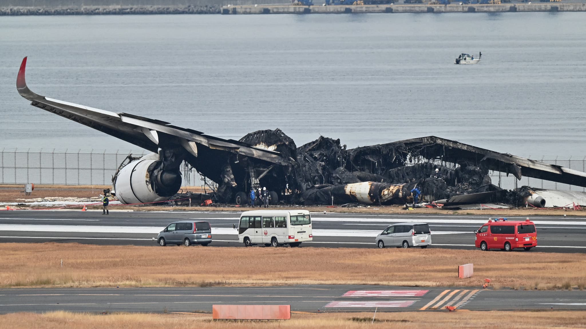 Des officiels regardent l'épave brûlée d'un avion de Japan Airlines sur le tarmac de l'aéroport international de Tokyo à Haneda à Tokyo le 3 janvier 2024, le matin après que l'avion ait percuté un plus petit avion des garde-côtes, faisant cinq morts.