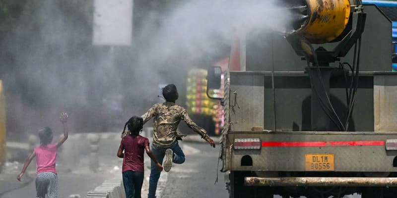 Des enfants courent derrière un camion pulvérisant de l'eau le long d'une rue par une chaude journée d'été à New Delhi, le 28 mai 2024.