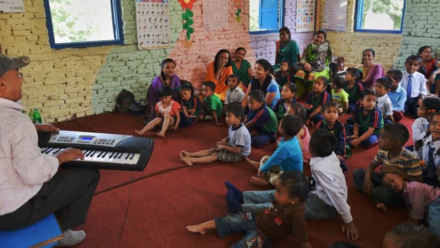 Un mois après le séisme dévastateur, des écoliers népalais entonnent une chanson autour de leur professeur, le 31 mai à Bhaktapur, près de Katmandu.