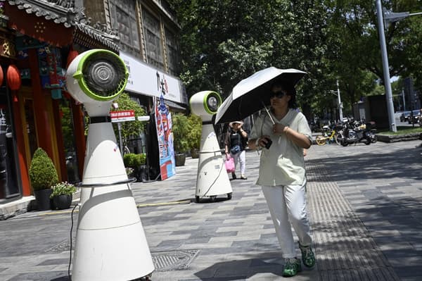Dans la rue, une femme se protège du soleil avec un parapluie devant un ventilateur de refroidissement, à Pékin, le 6 juillet 2023.