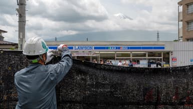 Un homme installant une bâche devant une vue du mont Fuji pour dissuader les touristes d'en prendre des photos, à Fujikawaguchiko, le 21 mai 2024