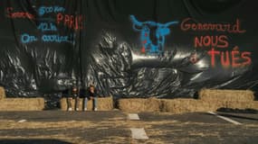 Des agriculteurs assis devant une bâche sur laquelle est écrit "Genevard nous a tués" (d) lors du blocage de l'autoroute A75 à Séverac-d'Aveyron, le 14 décembre 2025 dans l'Aveyron