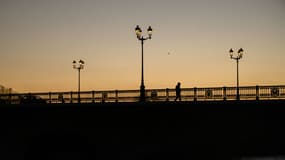 Un piéton traverse un pont alors que le soleil se couche à Toulouse, dans le sud de la France, le 13 janvier 2025.