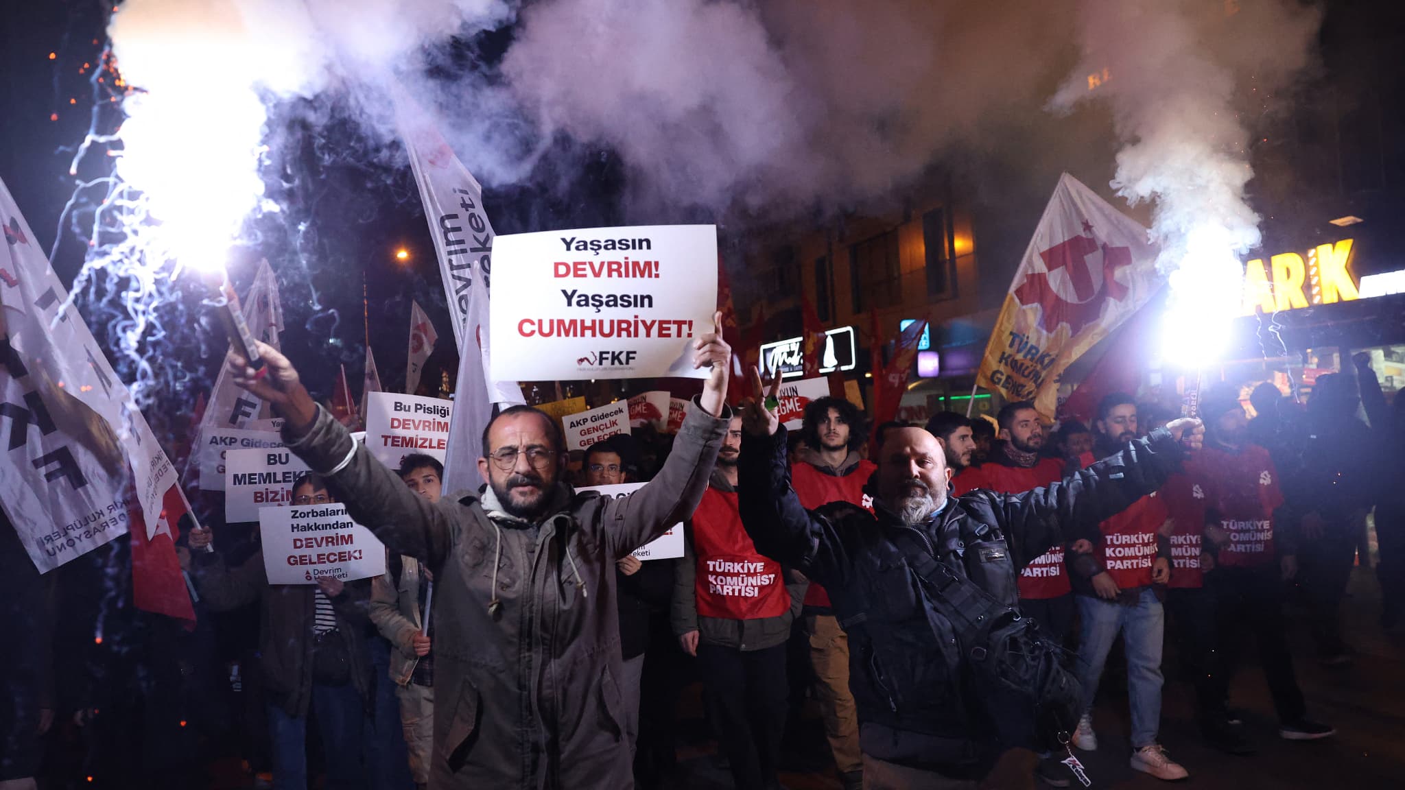Des manifestants allument des fusées éclairantes et tiennent une pancarte sur laquelle on peut lire « Vive la révolution, vive la république » lors d'un affrontement avec la police anti-émeute turque qui utilise des gaz lacrymogènes et des canons à eau lors d'une manifestation de soutien au maire d'Istanbul arrêté, à Ankara (Turquie), le 23 mars 2025.