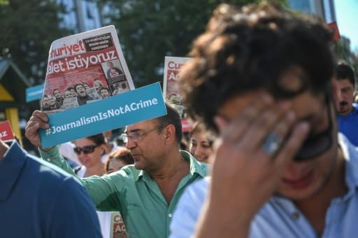 Un journaliste de Cumhuriyet brandit une pancarte avec le slogan "le journalisme n'est pas un crime", le 24 juillet 2017 devant le tribunal d'Istanbul Un journaliste de Cumhuriyet brandit une pancarte avec le slogan "le journalisme n'est pas un crime", le 24 juillet 2017 devant le tribunal d'Istanbul