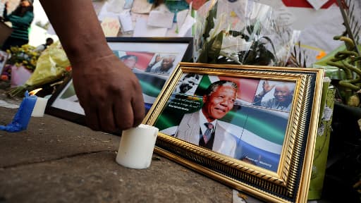 Un homme enflamme une bougie près des portraits de Nelson Mandela devant la clinique de Pretoria, le 11 juillet 2013.