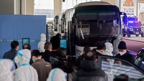 Des membres de l'équipe de l'Organisation mondiale de la santé (OMS) montent à bord d'un bus après leur arrivée dans une section bouclée de la zone des arrivées internationales de l'aéroport de Wuhan, le 14 janvier 2021.