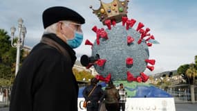 Un homme portant un masque passe près d'une sculpture à l'effigie du virus créée par des caravaliers à Nice, le 16 février 2021