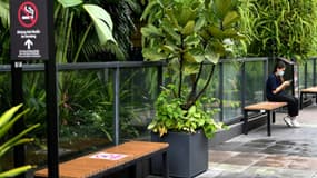 Une femme vérifie son smartphone assise sur un banc en respectant la distanciation sociale dans un centre commercial de Hanoi le 24 juin 2021 