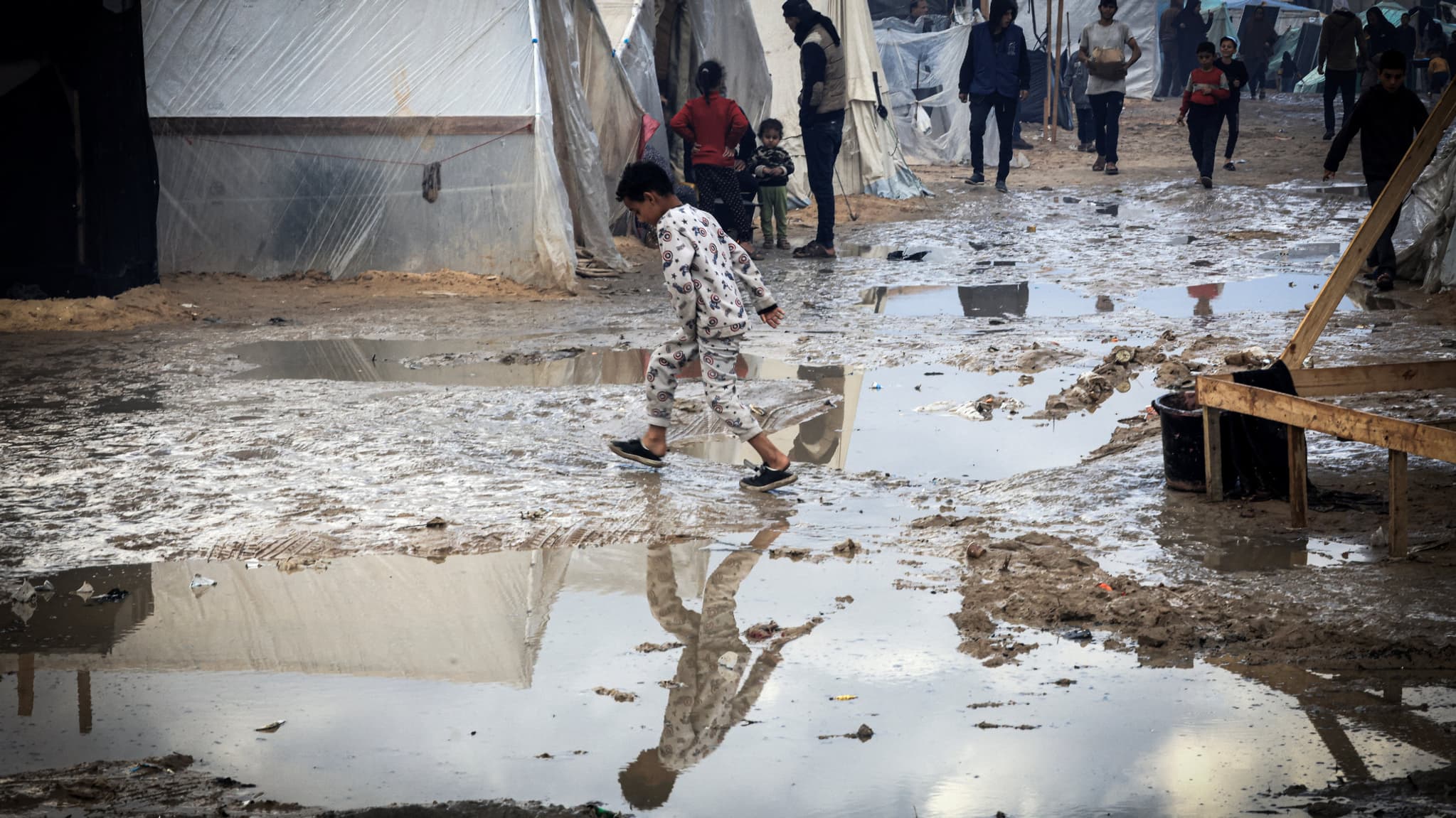 Un enfant palestinien marche en évitant les flaques dans un camp de Palestiniens fuyant les combats, à Rafah, dans la bande de Gaza, le 2 janvier 2024