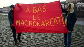 Des militantes féministes brandissent une banderole avec un jeu de mots entre le nom du président français Emmanuel Macron et le patriarcat pour lire « A bas la macronararchie » lors d'une manifestation contre le sexisme, devant le palais de justice de Nantes, dans l'ouest de la France, le 11 janvier 2024. 