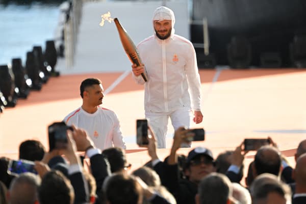 Le rappeur Jul tient la flamme olympique à la main, aux côtés du nageur Florent Manaudou, à leur arrivée sur le Vieux-Port de Marseille, le 8 mai 2024 