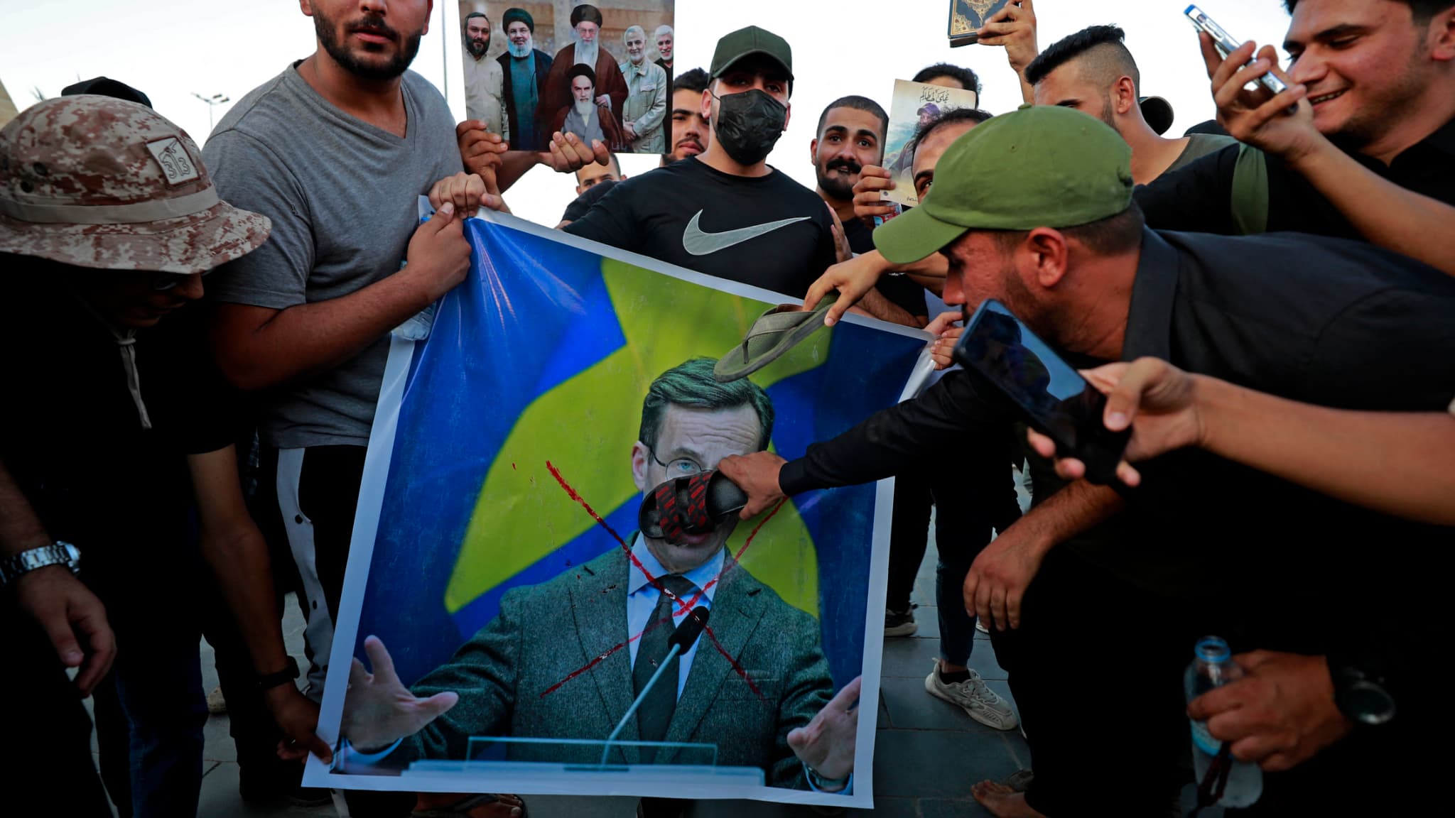Des partisans de l'ancien groupe paramilitaire Hashd al-Shaabi tiennent une affiche représentant le Premier ministre suédois Ulf Kristersson avec un grand X dessiné dessus lors d'une manifestation sur la place Tahrir de Bagdad le 20 juillet 2023.