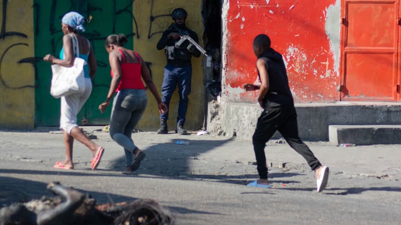 Des gens passent devant des corps brûlés et un officier de police armé surveillant une rue après des violences entre gangs dans le quartier dans la soirée du 21 mars 2024, à Port-au-Prince, Haïti, le 22 mars 2024. 