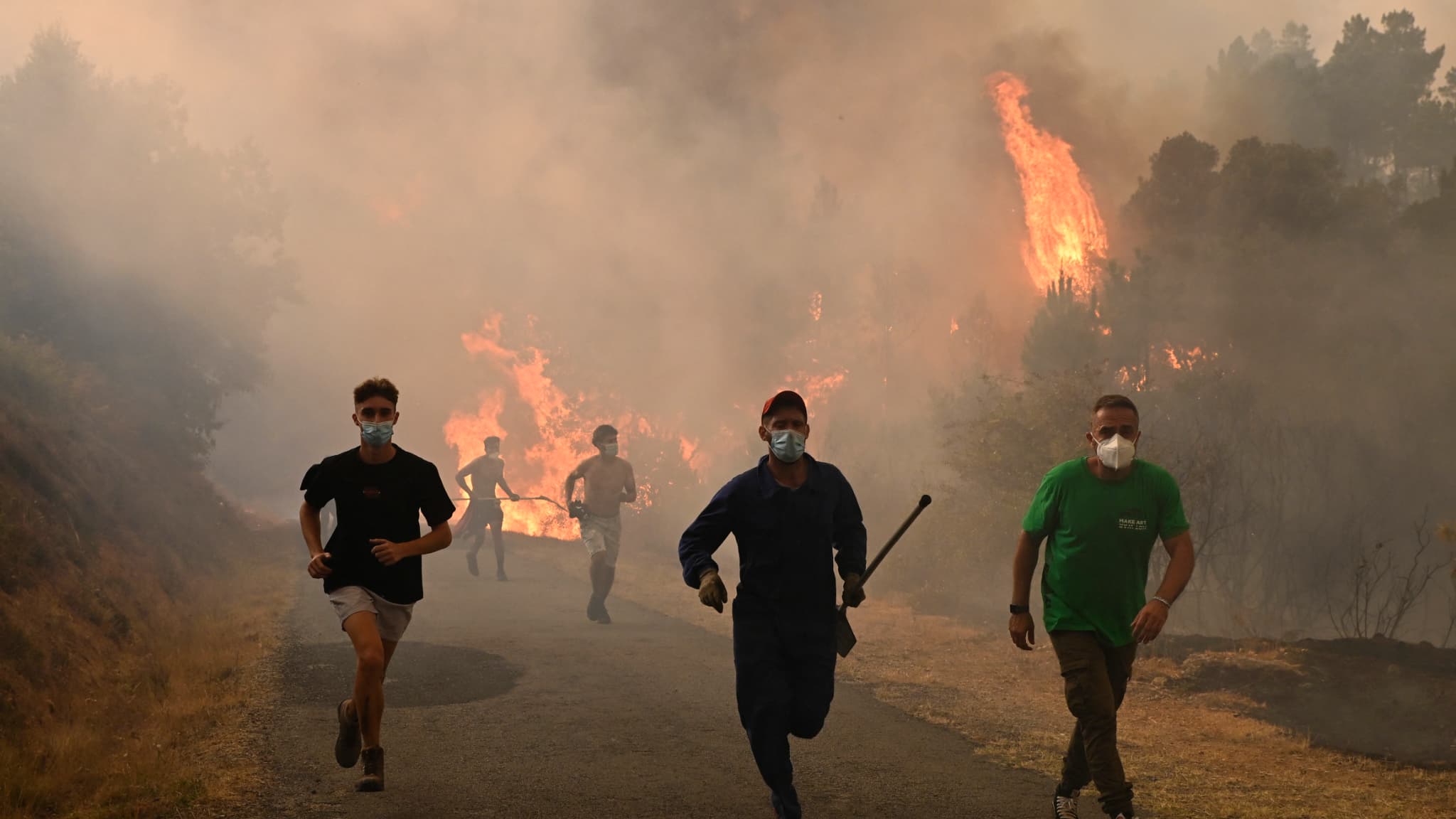 Des personnes courent près d'une zone incendiée lors d'un incendie de forêt près du village de Larouco, dans la province d'Ourense, au nord-ouest de l'Espagne, le 13 août 2025.