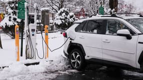 Une voiture électrique branchée à une borne de recharge, sous la neige.