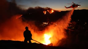 Des pompiers interviennent sur des maisons détruites tandis qu'un hélicoptère largue de l'eau alors que l'incendie de Palisades prend de l'ampleur à Pacific Palisades, en Californie, le 7 janvier 2025.