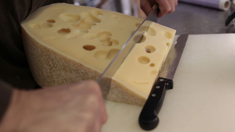 Un vendeur de fromages coupe une tranche d'emmental