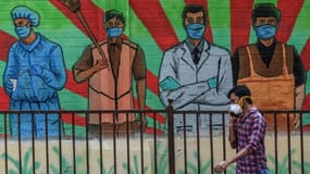 Un piéton portant un masque de protection passe devant une fresque murale représentant diverses professions mobilisées contre la pandémie de Covid-19, à Bombay (Inde) le 21 mars 2021