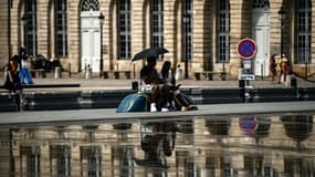 Un couple s'abrite du soleil sous une ombrelle près du miroir d'eau à Bordeaux, le 23 août 2023 en Gironde