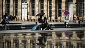 Un couple s'abrite du soleil sous une ombrelle près du miroir d'eau à Bordeaux, le 23 août 2023 en Gironde pendant la canicule