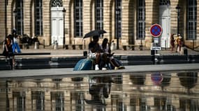 Un couple s'abrite du soleil sous une ombrelle près du miroir d'eau à Bordeaux, le 23 août 2023 en Gironde