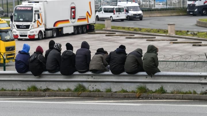 Des migrants sont assis sur une barrière près de la rocade du port de Calais le 30 mars 2018 