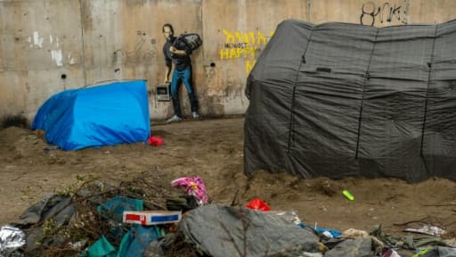 Des tentes de migrants devant une oeuvre de l'artiste britannique Bansky photographiée le 12 décembre 2015 et située à l'entrée de la "Jungle" de Calais, représente Steve Jobs (Apple), qui porte un baluchon et un vieil ordinateur