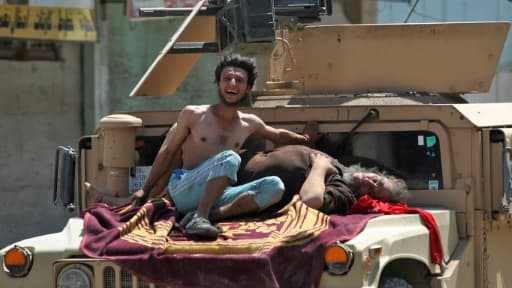 Des civils blessés lorsqu'un kamikaze s'est fait exploser, attendent des secours installés sur le capot d'un véhicule des forces de sécurité irakiennes, le 23 juin 2017 à Mossoul