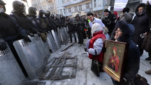 Des manifestants portant des icônes sont agenouillés face aux policiers anti-émeutes, le 24 janvier, à Kiev.