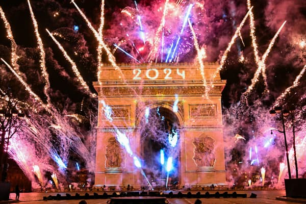 Des feux d'artifice explosent à côté de l'Arc de Triomphe avec "2024" projeté, sur l'avenue des Champs-Elysées pendant les célébrations du Nouvel An à Paris, au début du 1er janvier 2024.