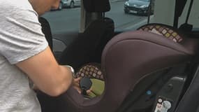 Un papa attache son siège bébé.