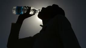 Une personne boit de l'eau à la bouteille en période de fortes chaleurs. 