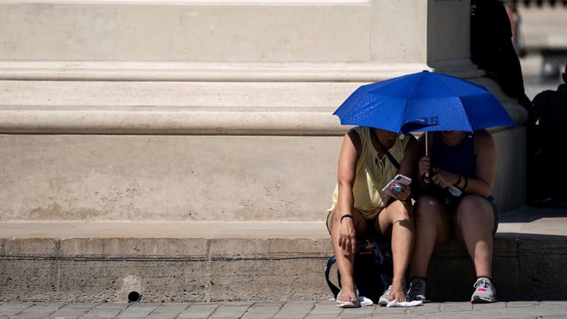 Des touristes s'abritant près de la pyramide du Louvre, pour échapper à la chaleur en juin 2019.