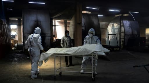 Des employés en combinaison protectrice près d'une civière où repose le corps d'une personne morte du coronavirus avant son incinération, le 3 juin 2020 au crématorium du site de Nigambodh Ghat à New Delhi Des employés en combinaison protectrice près d'une civière où repose le corps d'une personne morte du coronavirus avant son incinération, le 3 juin 2020 au crématorium du site de Nigambodh Ghat à New Delhi