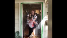 Une fillette installe un rideau en plastique devant chez ses grands-parents pour pouvoir les enlacer