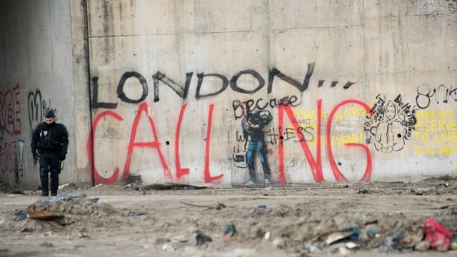 Un policier se tient près de graffitis durant le démantèlement de la partie sud de la "Jungle" de Calais, le 10 mars 2016. 