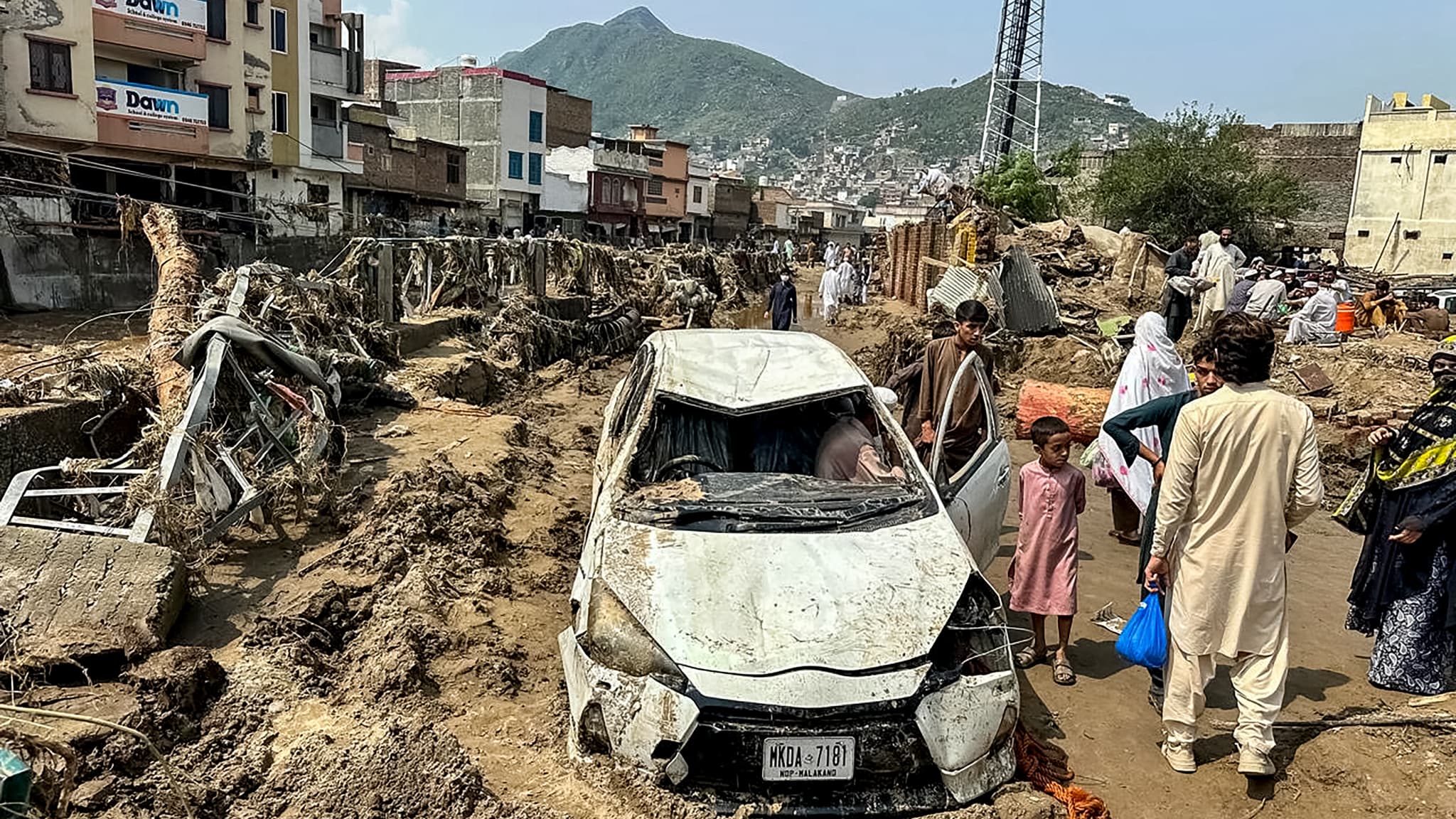 Des personnes se rassemblent près d'un véhicule endommagé et de débris éparpillés après que la route a été emportée par une crue soudaine à Mingora, la principale ville de la vallée de Swat, dans la province montagneuse de Khyber Pakhtunkhwa, touchée par la mousson, le 16 août 2025.