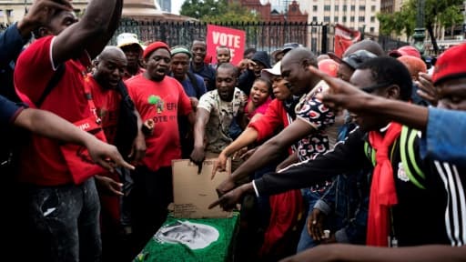 Des militants de l'opposition portent un faux cercueil avec la photo du président sud-africain Jacob Zuma lors d'un rassemblement pour exiger son départ, le 12 avril 2017 à Pretoria Des militants de l'opposition portent un faux cercueil avec la photo du président sud-africain Jacob Zuma lors d'un rassemblement pour exiger son départ, le 12 avril 2017 à Pretoria