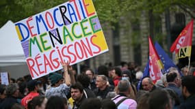 Un manifestant tient une pancarte sur laquelle on peut lire "Démocratie menacée, réagissons" lors d'une manifestation pour "défendre l'État de droit" à Paris, le 12 avril 2025, suite aux réactions à la condamnation Marine Le Pen. 
