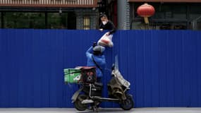 Un livreur passe des courses alimentaires au dessus d'une barrière d'un quartier résidentiel, à Pékin, le 11 mai 2022.