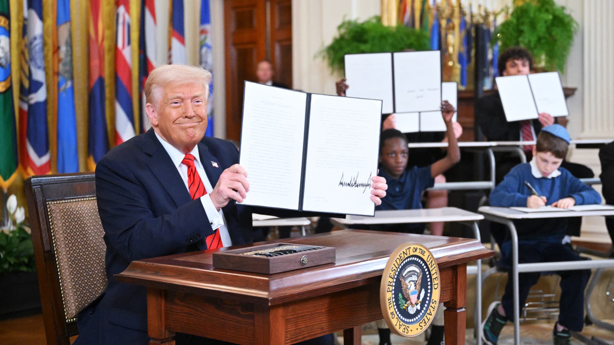 Le président américain Donald Trump montre le décret pour commencer à démanteler le ministère de l'Éducation après l'avoir signé dans une salle de la Maison Blanche remplie de tables d'écoliers à Washington, le 20 mars 2025