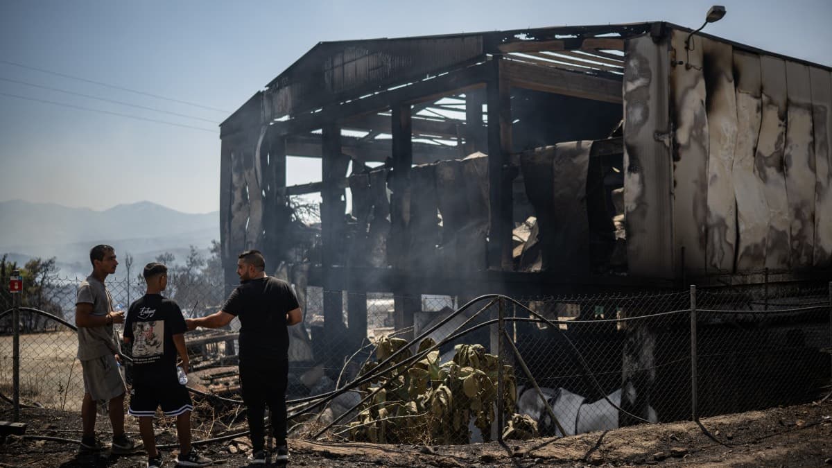 Des habitants se tiennent devant un abattoir incendié à la suite d'un incendie de forêt près du village de Psachna, en Grèce, le 27 juillet 2025. Des habitants se tiennent devant un abattoir incendié à la suite d'un incendie de forêt près du village de Psachna, en Grèce, le 27 juillet 2025.
