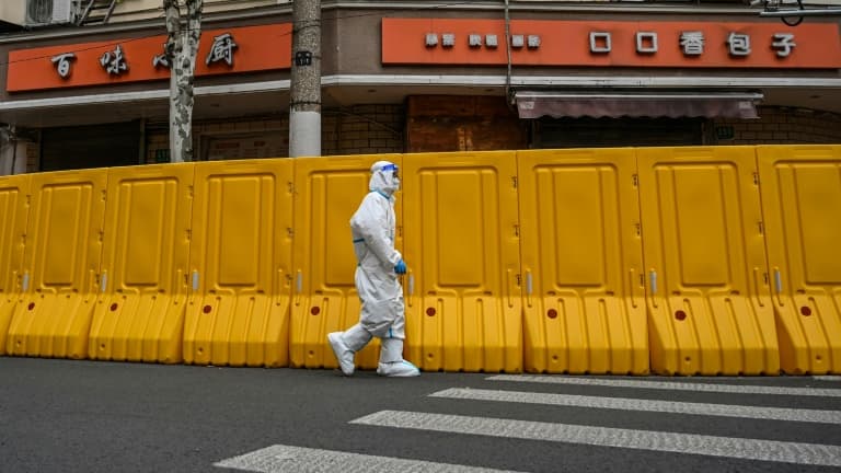 Un employé en tenue de protection passe devant une barrière isolant un quartier confiné pour lutter contre le Covid-19, à Shanghai en Chine le 30 mars 2022