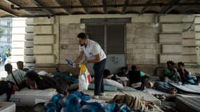 Un bénévole de l'ONG Médecins du Monde (MdM) distribue de l'eau en bouteille pour faire face aux fortes chaleurs lors d'une opération de maraude dans le camp de migrants du quartier Stalingrad à Paris le 12 juillet 2023. 
