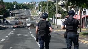 Des policiers en patrouille sur une rue bloquée par des objets incendiés et des débris, dans le quartier Magenta à Nouméa en Nouvelle-Calédonie, le 18 mai 2024