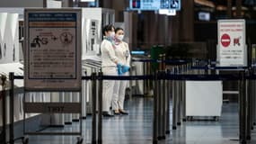 Des hôtesses portant des masques et gants de protection contre le Covid-19 se tiennent près d'une porte d'embarquement à l'aéroport Haneda de Tokyo, le 29 novembre 2021