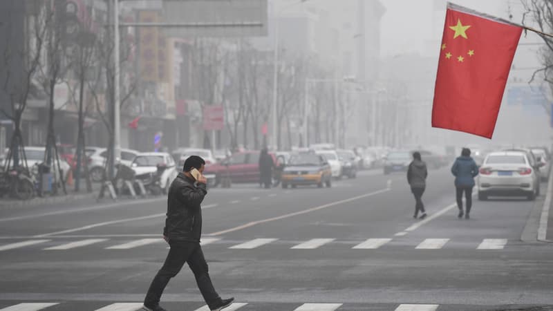 Un homme traverse une route sous le drapeau national chinois lors d'une journée très polluée à Shijiazhuang, dans la province du Hebei, dans le nord de la Chine, le 21 décembre 2016.