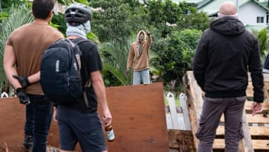 Des habitants masqués regardent un activiste à l'entrée du quatrier de Tuband, à Nouméa, le 15 mai 2024