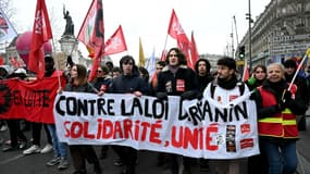 Des gens défilent derrière une banderole lors d'une manifestation contre la loi sur l'immigration récemment votée, place de la République, dans le centre de Paris, le 14 janvier 2024.